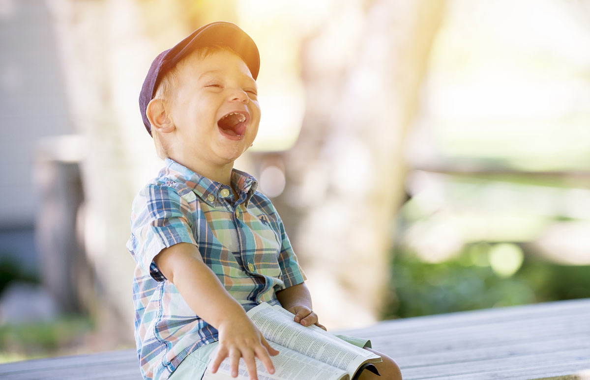 A child laughing with a book at Apple Valley Childcare & Preschool