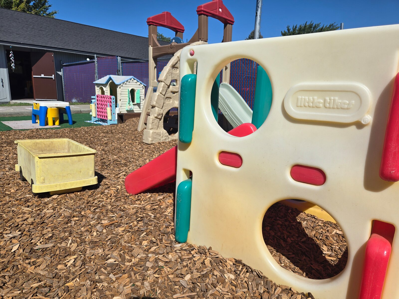 Apple Valley's play yard with a climbing frame and slide, a wooden play fort, a playhouse and giant Connect Four