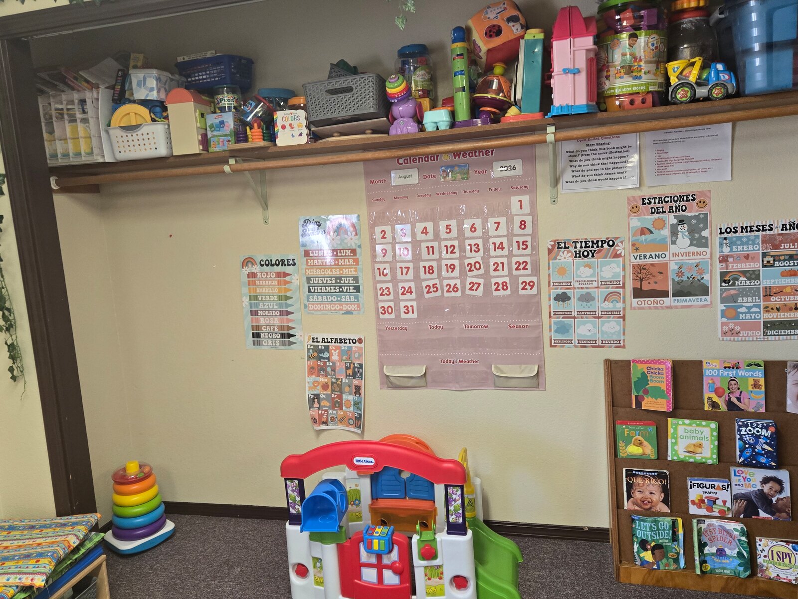 The Apple Valley toddler room with a Little Tikes activity centre, board books and a Spanish calendar and weather chart