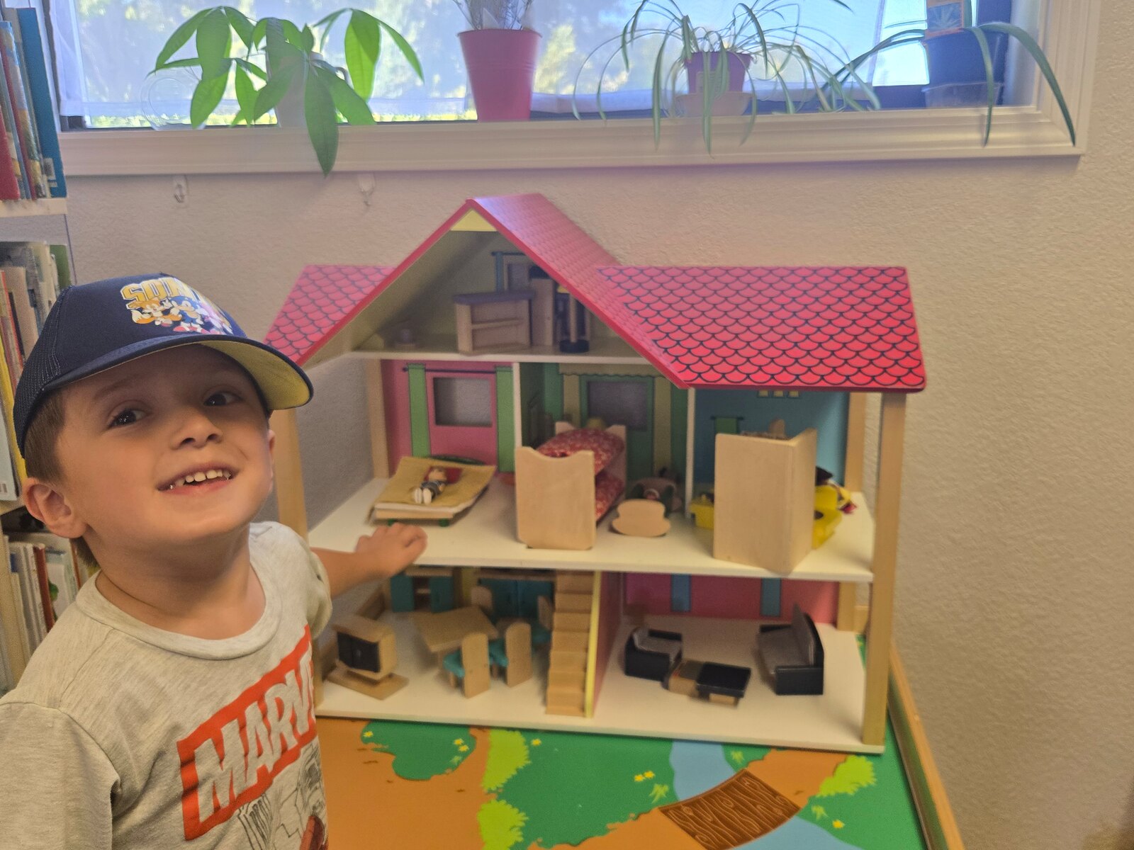 A preschooler smiling while playing at the wooden dollhouse in the Apple Valley classroom