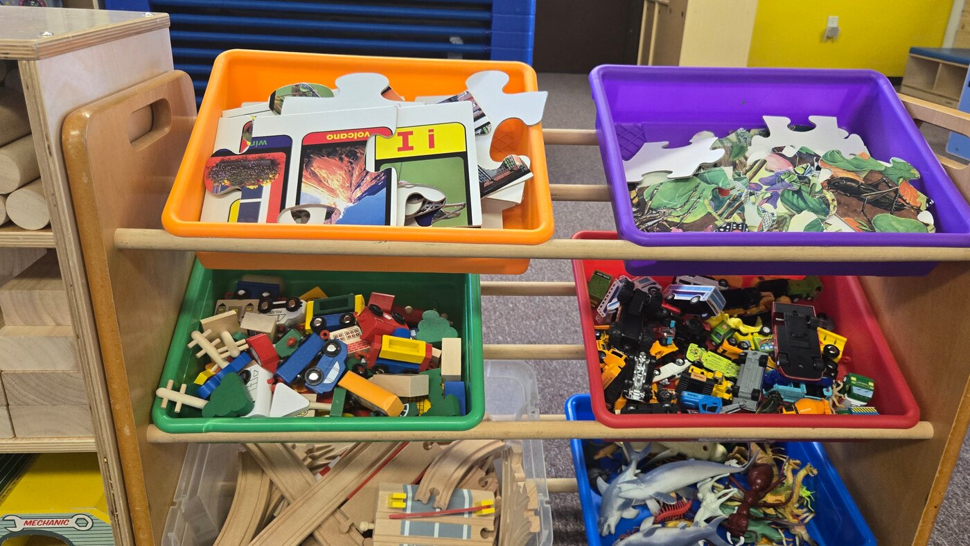 Colour-sorted bins of puzzles, blocks, vehicles and animals on an open Apple Valley shelf